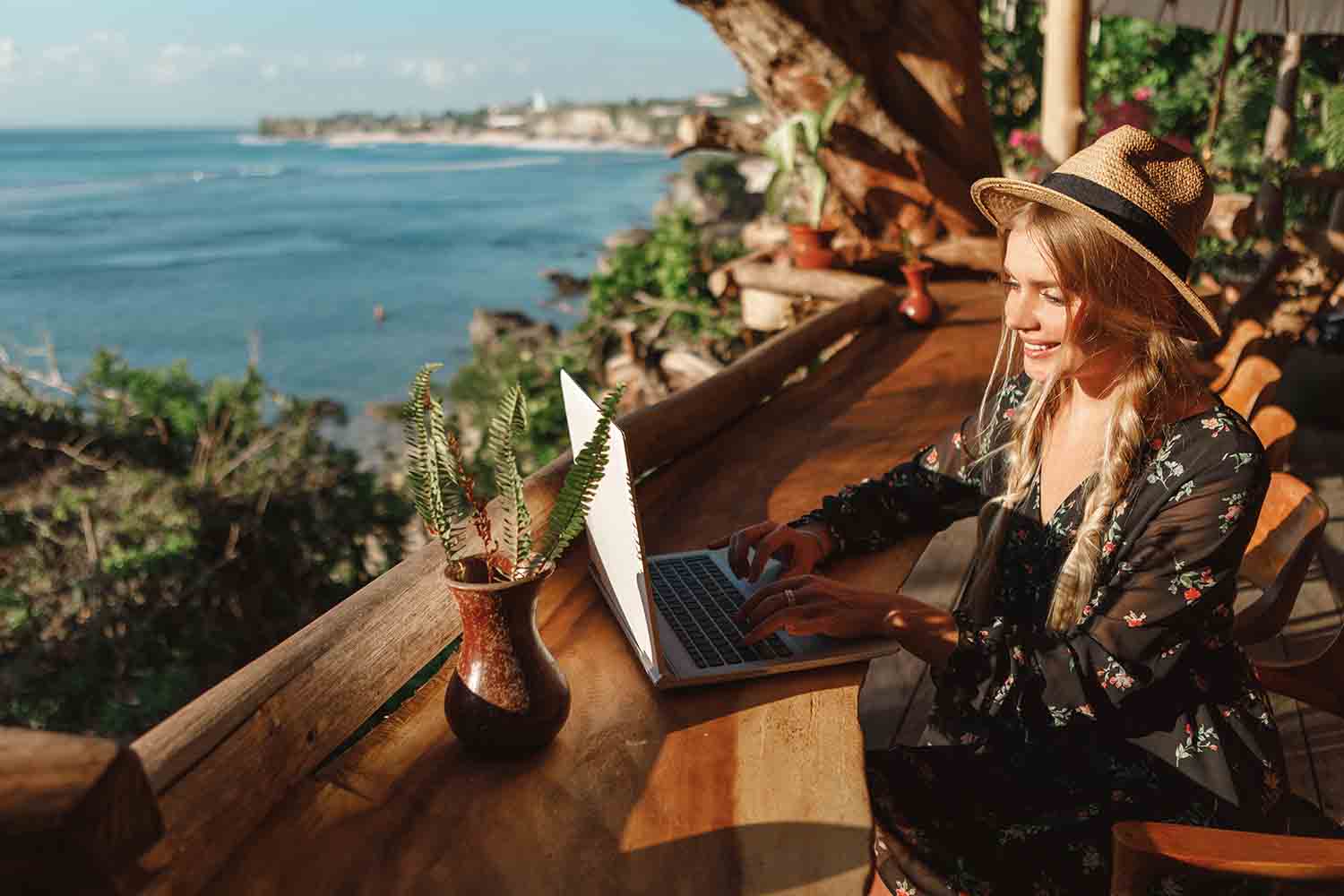 Симпатичная молодая женщина использует ноутбук в кафе на тропическом пляже на открытой террасе кафе с видом на море