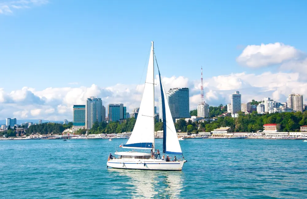 Белая парусная яхта в море на фоне города