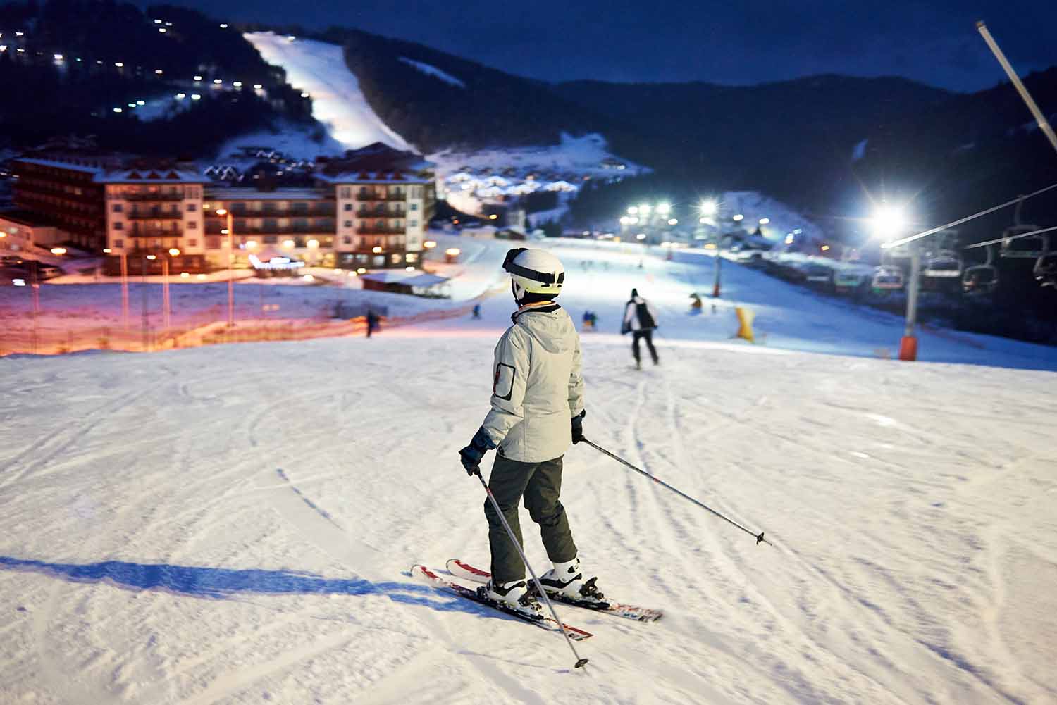 Лыжница смотрит на спуск горы в вечернее время
